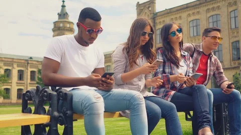 Friends sitting on benchand texting on cell phones Stock Footage 130051613