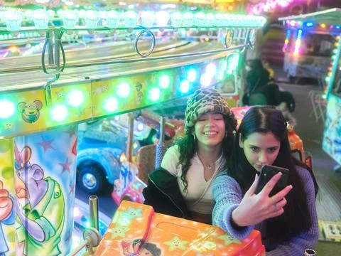 Friends sitting on a fairground attraction while taking a selfie at night Stock Photos