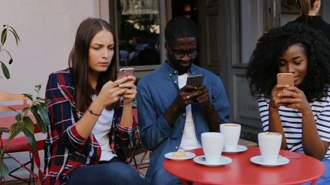 Friends sitting at red table on terrace in cafe and looking at smartphones Stock Footage 81836501