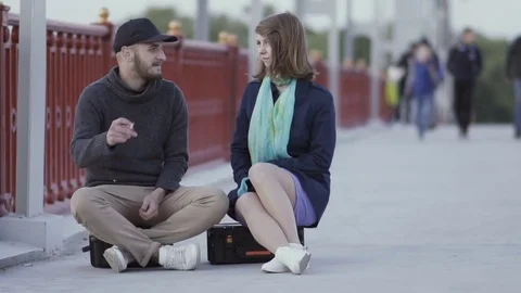 Friends sitting on suitcases on the bridge and talking Stock Footage