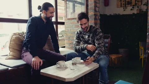 Friends smiling while looking at mobile phone in a cafe 스톡 동영상 95903460