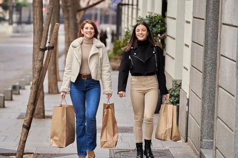 Friends smiling while walking down the street with shopping bags. Fotos Stock