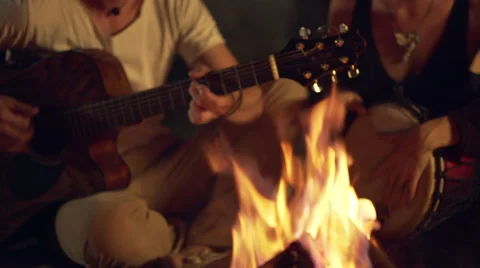Friends speaking, smiling, playing on instruments, sitting near bonfire at night Stock Footage 67108799