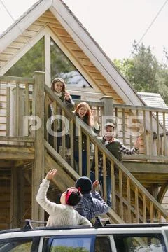 Friends on stairs waving to friends in car outside sunny cabin Stock Photos