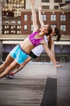 Friends stretching while exercising at park against building in city Fotos de archivo