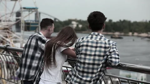 Friends, students stand in a walking area with a Ferris wheel, leaning on a Stock Footage 130538650