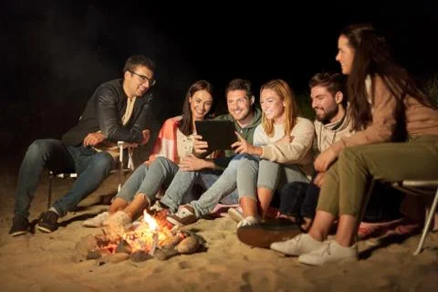 Friends with tablet pc at fire on beach at night Stock Photos