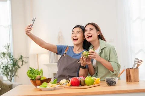Friends take selfie in kitchen while preparing fresh fruit and vegetables f.. Stock Photos