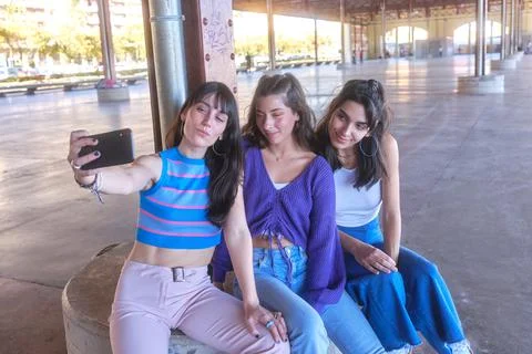 Friends taking a selfie with the mobile while sitting on an urban area Stock Photos