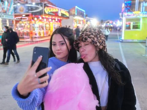 Friends taking selfie while grimacing and holding a cotton candy in a night fair Stock Photos