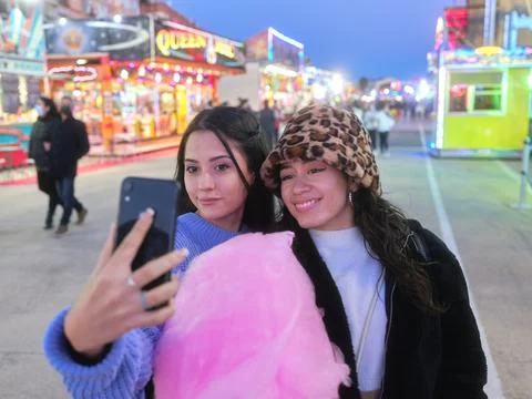 Friends taking selfie while holding a cotton candy in a night fair Stock Photos