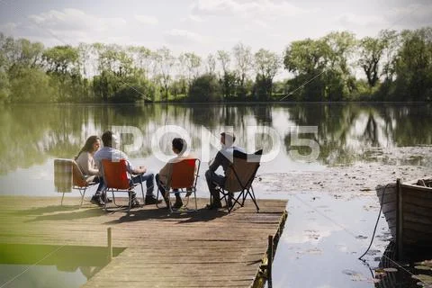 Friends talking hanging out at sunny lakeside dock Stock Photos