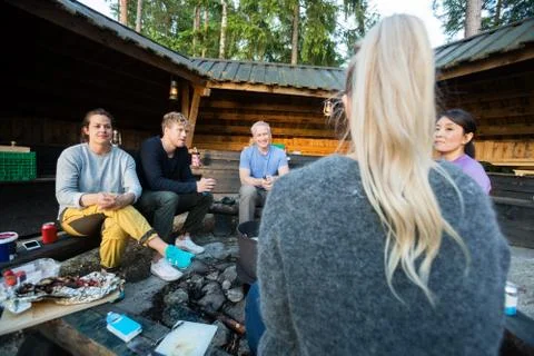 Friends Talking While Sitting By Firepit Outside Shed Foto stock