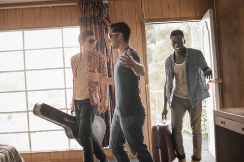 Friends, three young men in a motel room, carrying cases and a guitar. Stock Photos