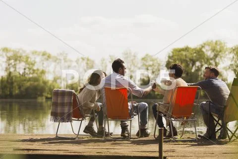 Friends toasting coffee mugs at sunny lakeside dock Stock Photos