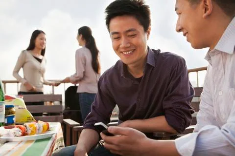 Friends Using Cell Phone at Rooftop Barbecue Stock Photos