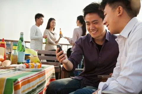 Friends Using Cell Phone at Rooftop Barbecue Stock Photos