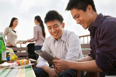 Friends Using Digital Tablet at Rooftop Barbecue Stock Photos