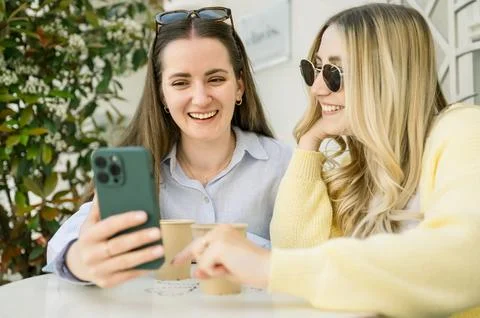 Friends using phone drinking take away coffee in a cafe Stock Photos