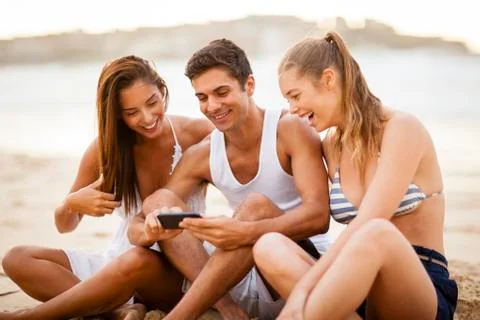 Friends using a smart phone on the beach Stock Photos