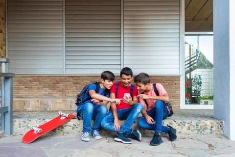 Friends using smart phone while sitting against school building Fotos de archivo