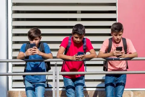 Friends using smart phones while standing by railing in school building during Fotos de archivo