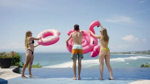 Friends walks along the infinity pool with inflatable pink flamingo, rubber ring Stock Footage 269121161