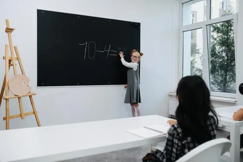 Frienly schoolgirl solving a basic math equasion on a blackboard in a class Stock Photos