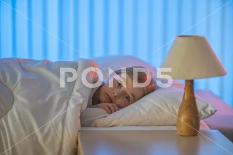 The frightened girl lay on the bed. Evening night time Stock Photos