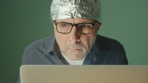 A Frightened Man in a Foil Cap Sitting at a Laptop, Anxiously Looking Around. 動画素材 166650857