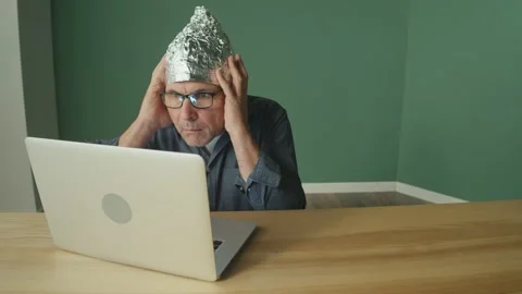 A Frightened Man in a Foil Cap Sitting at a Laptop, Anxiously Looking Around. 스톡 동영상 166705319