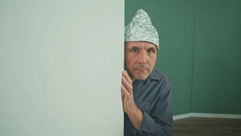 A Frightened Man in a Protective Foil Cap Peeking Strangely Around the Corner Stock Footage 166650317