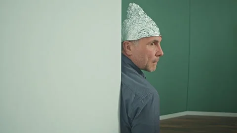 A Frightened Man in a Protective Foil Cap Peeking Strangely Around the Corner Stock Footage 166706703