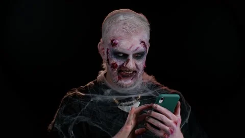 Frightening man Halloween zombie using mobile phone typing new post on web Stock Footage 161908159