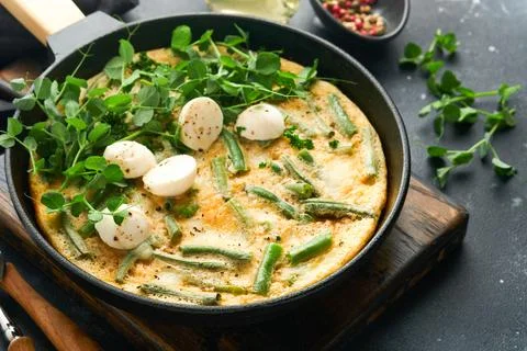 Frittata. Omelet with spinach and green beans, healthy food in black frying p Stock Photos