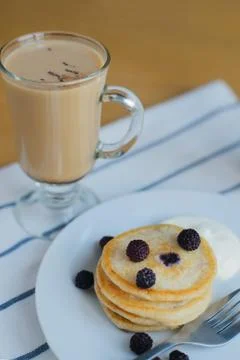 Fritter or pancakes with black raspberry, smetana, fork on plate and cappuccino Stock Photos