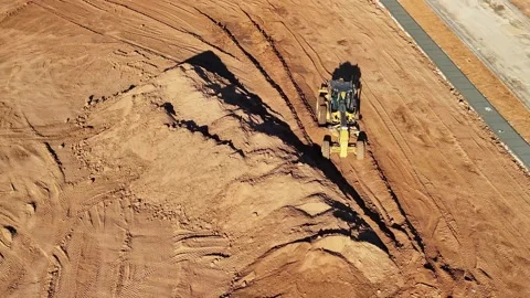 Front on aerial view of a grader moving along amongst piles of dirt Stock Footage 278340240