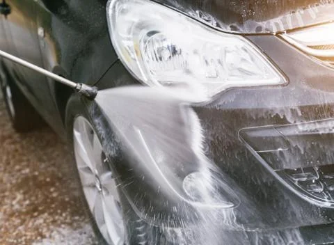 Front of black car gets cleaned by steam radiator at DIY car wash. Stock Photos