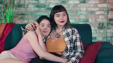 In front of the camera pretty looking lesbian couple ladies sitting on the sofa Stock Footage 229782401