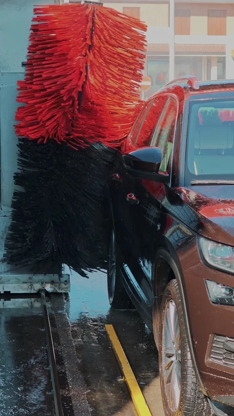 Front corner of SUV washed by rotating brush, wet floor and soapy water around Stock Footage 330784176