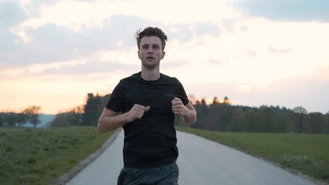 Front dolly of man athlete running on street between meadows, slow motion Stock Footage 129610377
