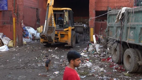 Front end loader shovels piles of garbage onto truck as pedestrians pass by Stock Footage 96313575
