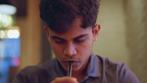 Front-facing close-up of young man in buttoned shirt drinking from straw 動画素材 318244899