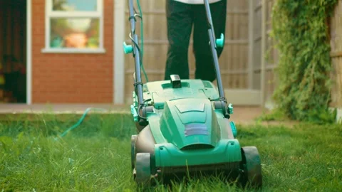 Front facing electric lawn mower cutting long grass in residential garden Stock Footage 314826990