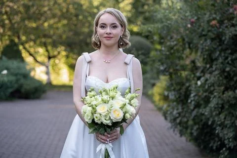 Front-facing portrait of a bride in a white tea-length wedding dress, gently hol Stock Photos