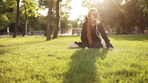 Front footage of cheerful red headed lady in sunglasses sitting on the grass Stock Footage 114614082