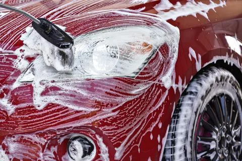 Front head light of red car washed in self serve carwash, brush leaving white Stock Photos