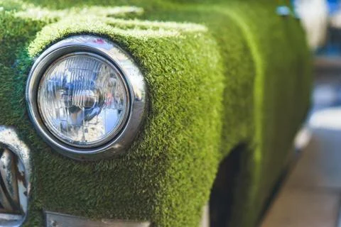 Front headlight of an old car in summer covered with artificial grass. Deco.. Foto stock