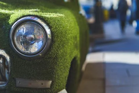 Front headlight of an old car in summer covered with artificial grass. Deco.. Stock Photos