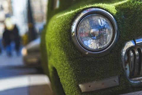 Front headlight of an old car in summer covered with artificial grass. Deco.. Stock Photos